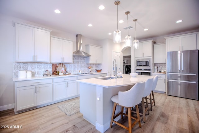 kitchen with wall chimney range hood, light countertops, arched walkways, a sink, and appliances with stainless steel finishes