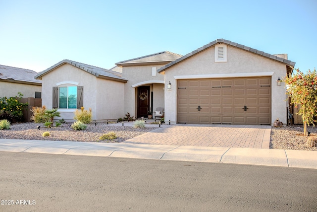 ranch-style house featuring a tiled roof, decorative driveway, a garage, and stucco siding