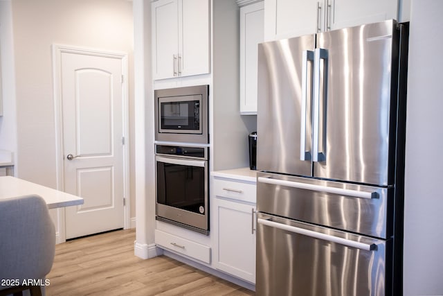 kitchen featuring appliances with stainless steel finishes, light countertops, baseboards, white cabinets, and light wood finished floors
