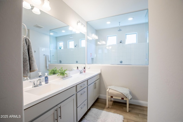 bathroom featuring double vanity, walk in shower, a sink, and wood finished floors