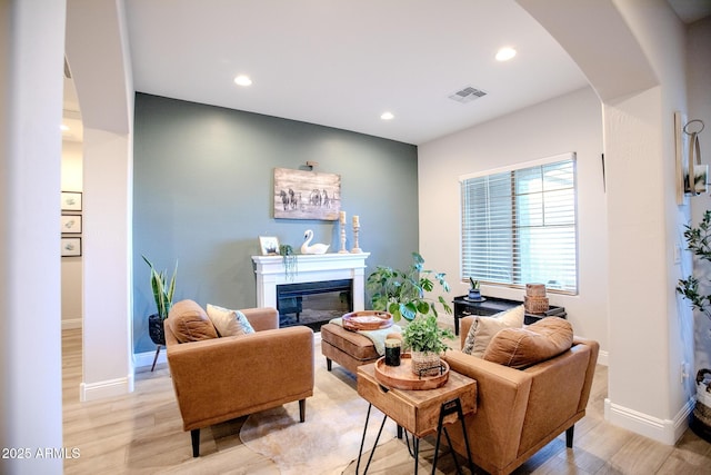 living area with visible vents, arched walkways, baseboards, light wood finished floors, and a glass covered fireplace