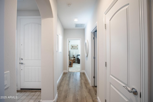 hallway featuring arched walkways, baseboards, visible vents, and light wood finished floors