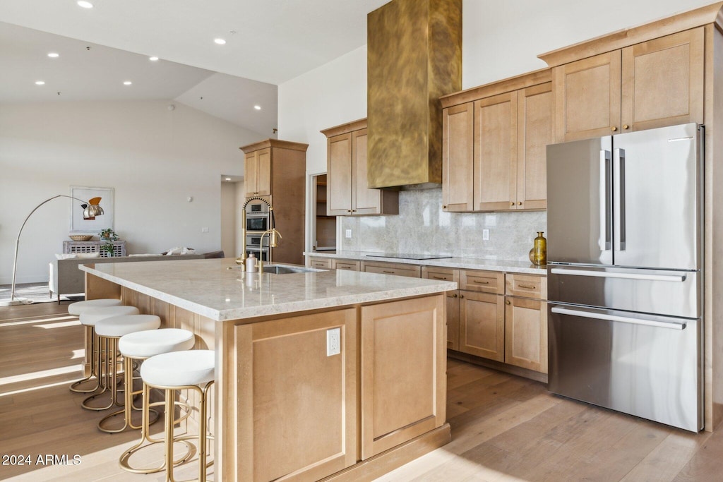 kitchen featuring stainless steel appliances, light stone countertops, a center island with sink, and a kitchen bar