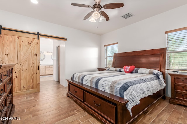 bedroom with hardwood / wood-style floors, ensuite bathroom, ceiling fan, and a barn door