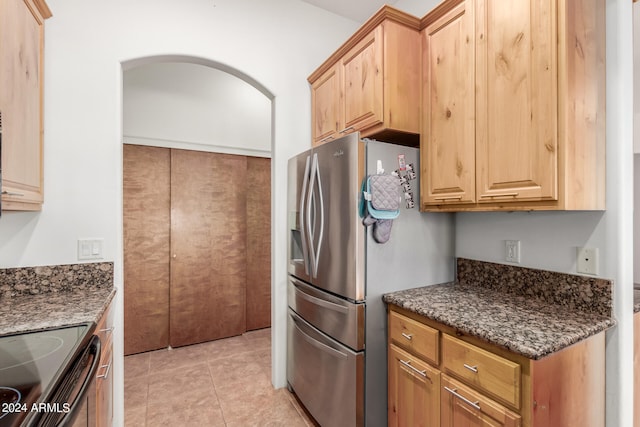 kitchen featuring stainless steel fridge with ice dispenser, dark stone counters, and light tile floors