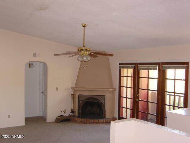 unfurnished living room featuring carpet floors, lofted ceiling, a large fireplace, and ceiling fan