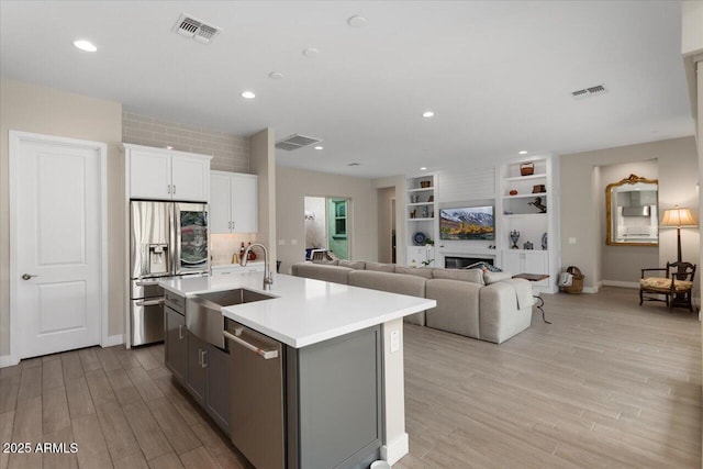 kitchen with white cabinets, sink, a fireplace, an island with sink, and stainless steel appliances