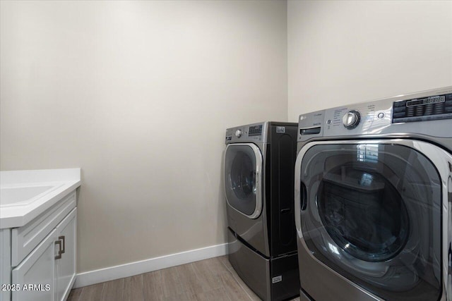 clothes washing area featuring cabinets, sink, light hardwood / wood-style floors, and independent washer and dryer