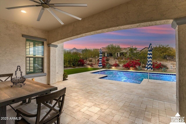 pool at dusk with a patio and ceiling fan