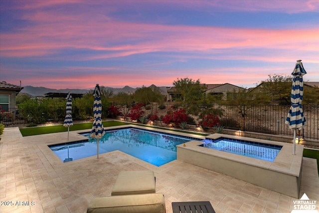 pool at dusk with a mountain view, an in ground hot tub, and a patio