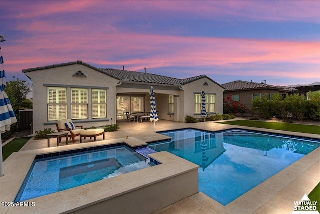 pool at dusk featuring a patio area and an in ground hot tub