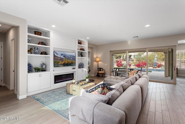 living room with built in shelves, light hardwood / wood-style floors, and a healthy amount of sunlight