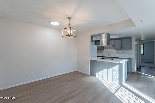 2440 N 22nd Ave, Phoenix, AZ 85009 - kitchen with wall chimney range hood, a sink, wood finished floors, light countertops, and a peninsula