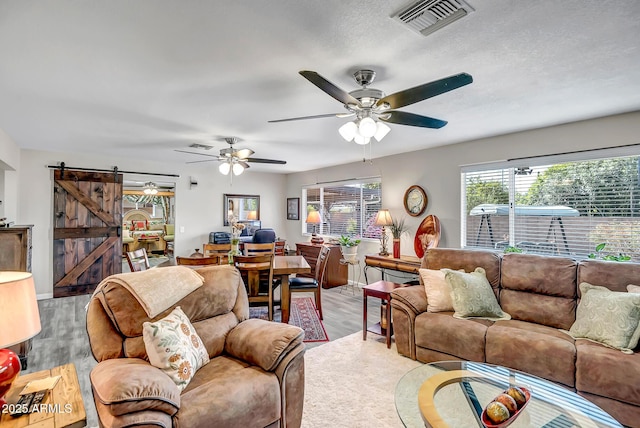 living room with visible vents, a ceiling fan, a barn door, and wood finished floors