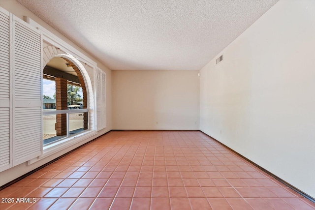 empty room featuring light tile patterned floors, baseboards, a textured ceiling, and visible vents