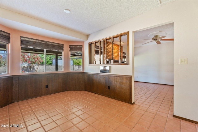 kitchen featuring light tile patterned flooring, wainscoting, a textured ceiling, wood walls, and a ceiling fan