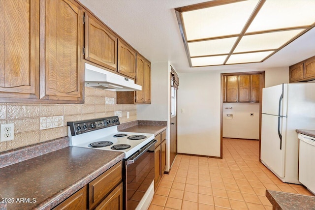 kitchen featuring brown cabinetry, dark countertops, tasteful backsplash, under cabinet range hood, and white appliances