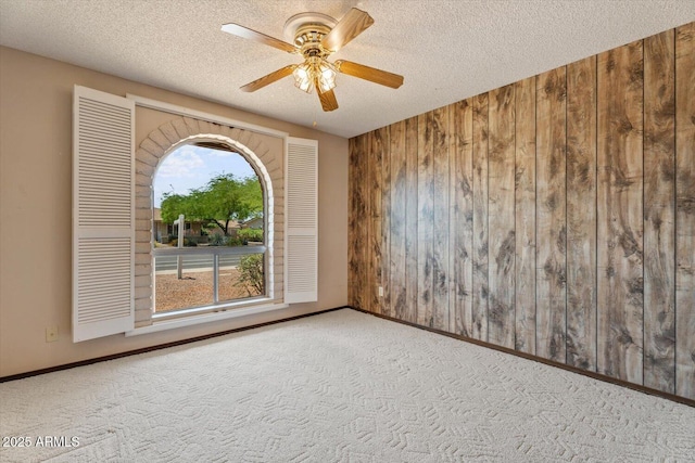 unfurnished room featuring carpet floors, wood walls, a textured ceiling, and ceiling fan