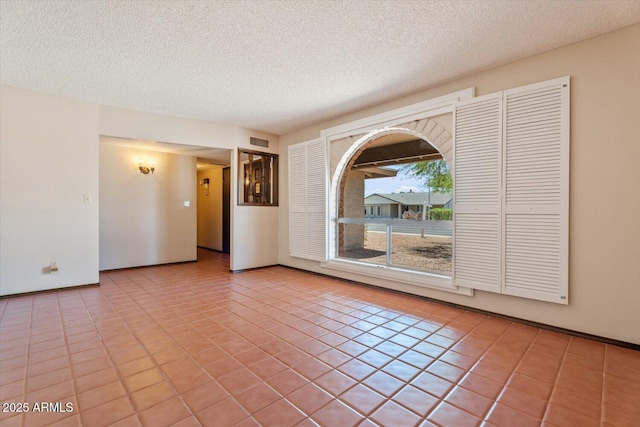 empty room featuring a textured ceiling, visible vents, baseboards, and tile patterned flooring
