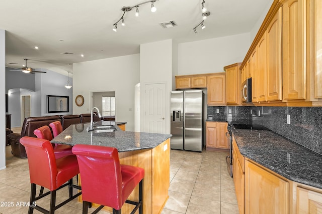 kitchen with light tile patterned floors, a breakfast bar, dark stone countertops, stainless steel appliances, and a center island with sink