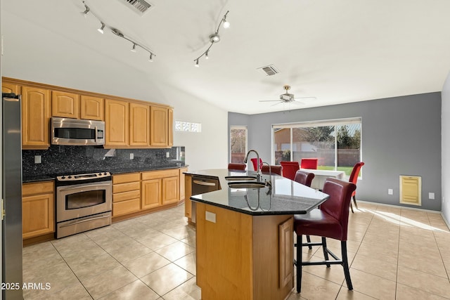 kitchen with sink, light tile patterned floors, appliances with stainless steel finishes, an island with sink, and decorative backsplash