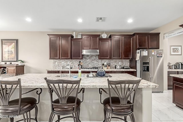 kitchen featuring visible vents, high quality fridge, tasteful backsplash, and under cabinet range hood