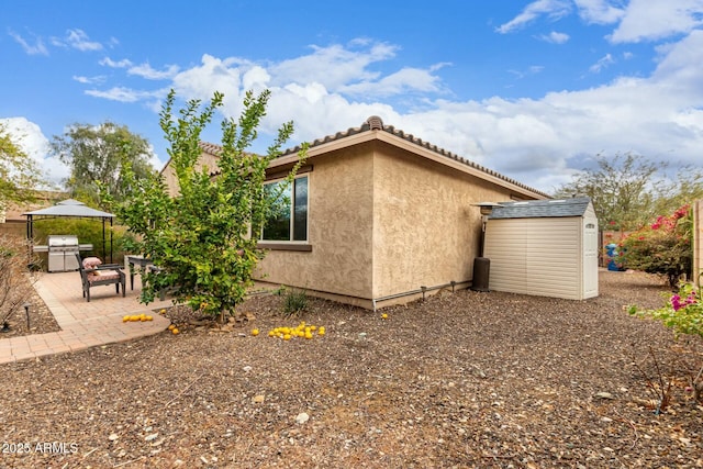 view of home's exterior with a storage unit, a patio, an outbuilding, and stucco siding