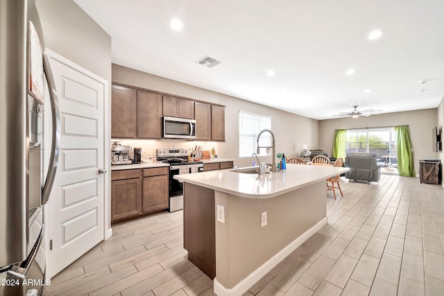 kitchen with light hardwood / wood-style floors, sink, a center island with sink, appliances with stainless steel finishes, and ceiling fan