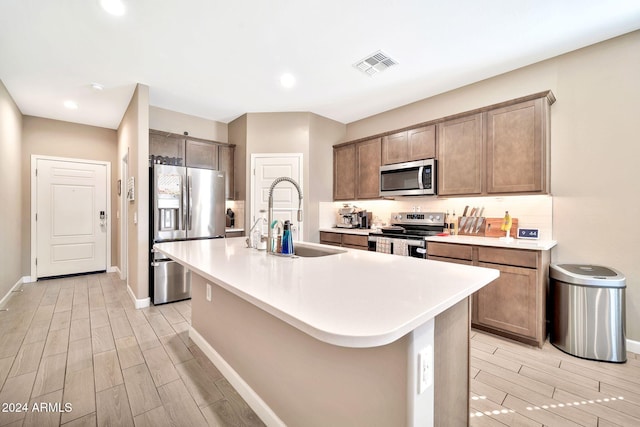 kitchen with appliances with stainless steel finishes, light hardwood / wood-style floors, a kitchen bar, a center island with sink, and sink