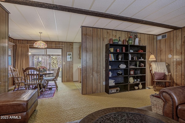 carpeted living room featuring beamed ceiling and wood walls