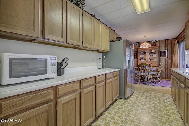 kitchen with decorative light fixtures, stainless steel refrigerator with ice dispenser, and wooden walls