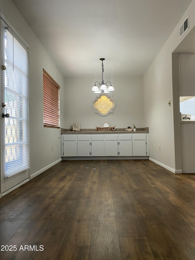 unfurnished dining area featuring a chandelier, baseboards, dark wood finished floors, and visible vents