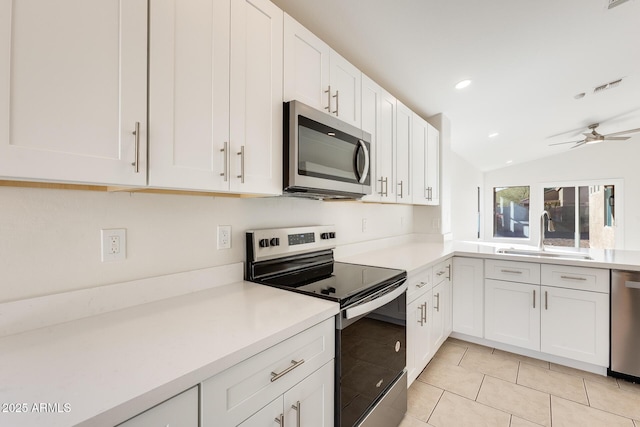 kitchen with lofted ceiling, sink, white cabinetry, light tile patterned floors, and appliances with stainless steel finishes