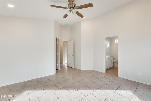 unfurnished bedroom with connected bathroom, light tile patterned floors, a towering ceiling, and ceiling fan