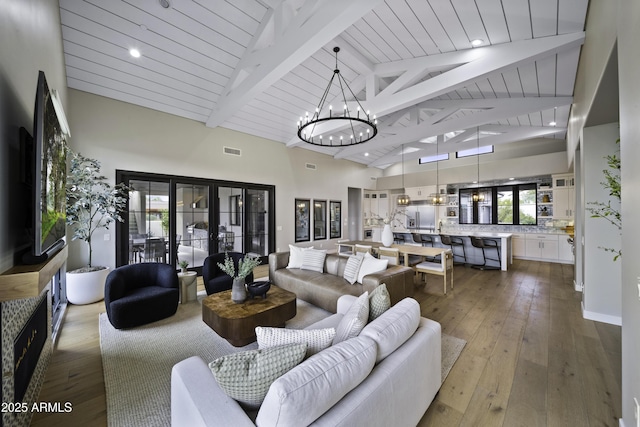 living room featuring hardwood / wood-style floors, beam ceiling, high vaulted ceiling, french doors, and a chandelier