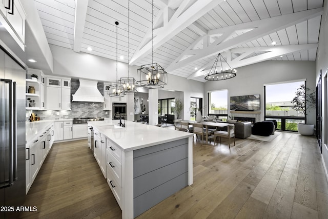 kitchen featuring tasteful backsplash, white cabinetry, wood-type flooring, custom exhaust hood, and a center island with sink