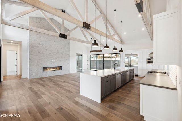 kitchen with stainless steel appliances, high vaulted ceiling, a large island with sink, pendant lighting, and a fireplace