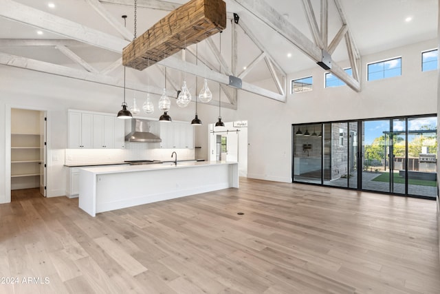 unfurnished living room with a barn door, beamed ceiling, high vaulted ceiling, and light hardwood / wood-style floors