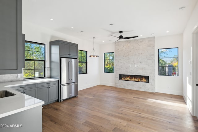 kitchen with pendant lighting, stainless steel fridge, gray cabinets, light wood-type flooring, and a stone fireplace