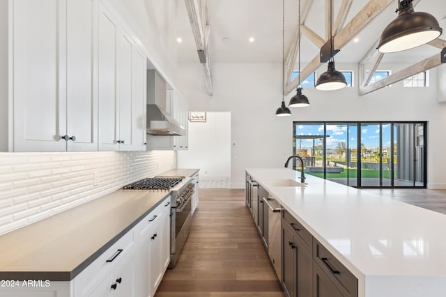 kitchen featuring white cabinets, appliances with stainless steel finishes, wall chimney exhaust hood, decorative light fixtures, and dark hardwood / wood-style floors