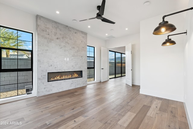 unfurnished living room with a stone fireplace, ceiling fan, and light wood-type flooring