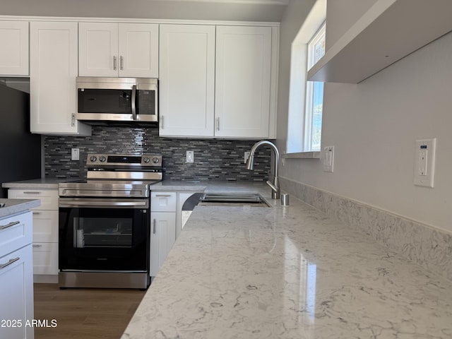 kitchen with light stone counters, a sink, stainless steel appliances, white cabinetry, and decorative backsplash
