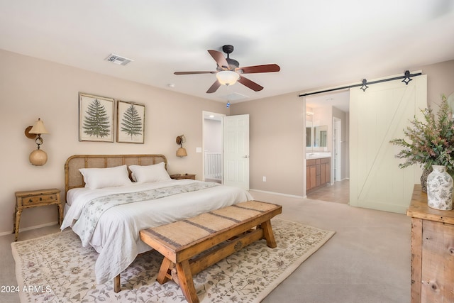 carpeted bedroom with a barn door, connected bathroom, and ceiling fan