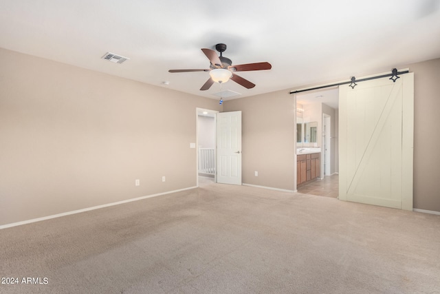 carpeted spare room featuring ceiling fan and a barn door