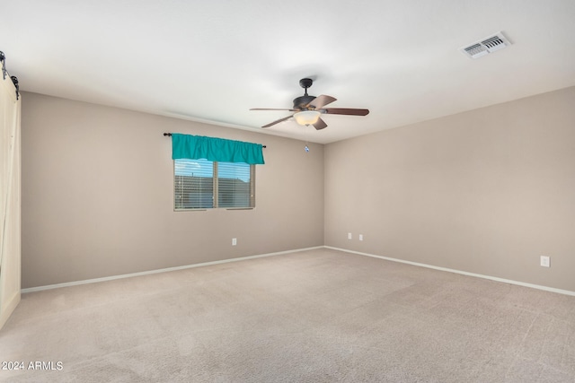 carpeted empty room with ceiling fan and a barn door