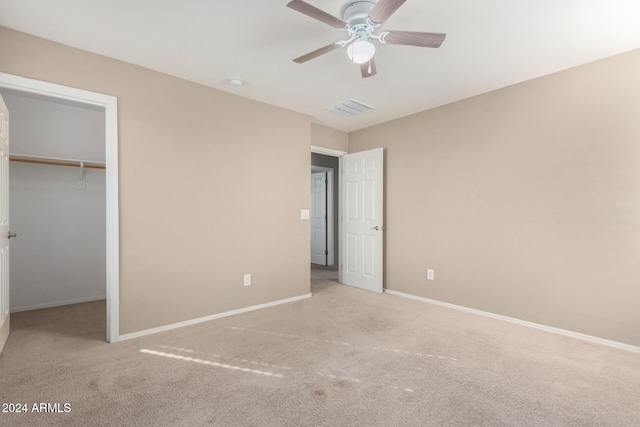 unfurnished bedroom featuring light carpet, a spacious closet, ceiling fan, and a closet