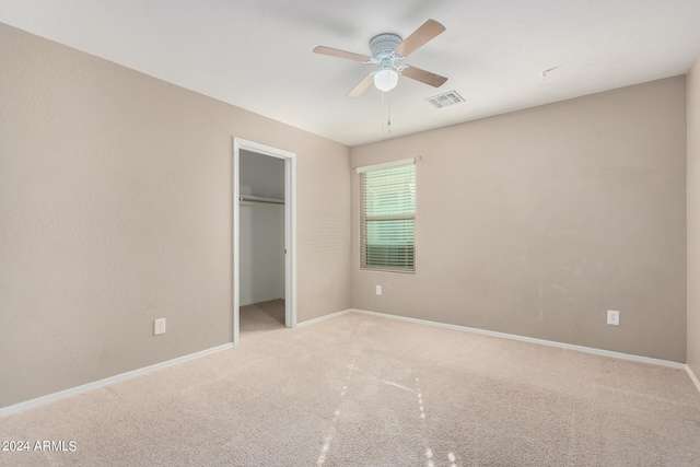 unfurnished bedroom featuring light carpet, a spacious closet, ceiling fan, and a closet