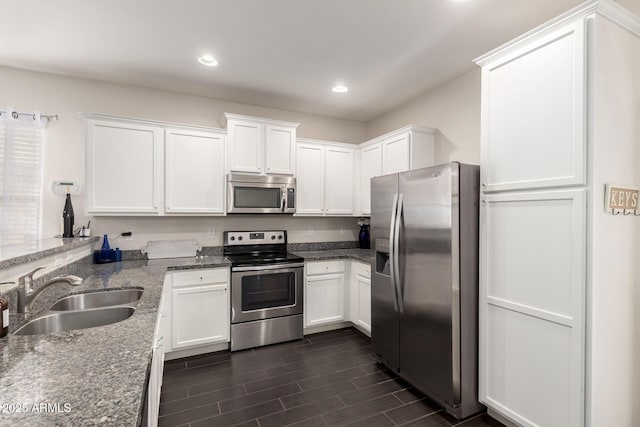 kitchen featuring white cabinetry, stainless steel appliances, a sink, and dark stone counters