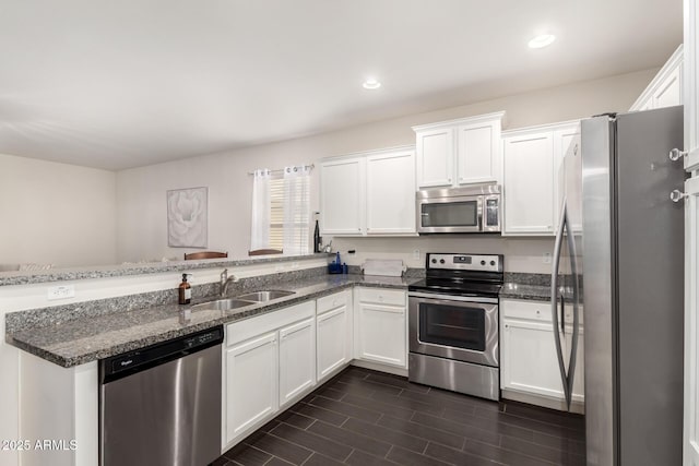 kitchen with a peninsula, white cabinetry, appliances with stainless steel finishes, and a sink