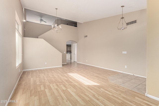 unfurnished living room with visible vents, a chandelier, wood finished floors, arched walkways, and high vaulted ceiling